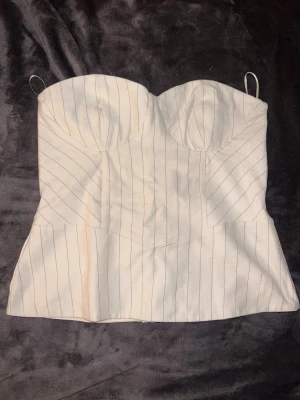 Vit randig korsett från Bershka - Säljer en vit korsett från Bershka med tunna svarta ränder. Toppen har snörning i ryggen och dragkedja i sidan💕 Aldrig använd 