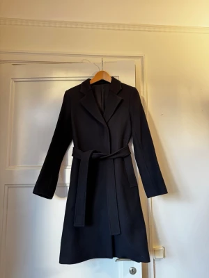 Kappa Filippa k  - Skräddarsydd omlottkappa med klassisk passform, tillverkad av italienskt kostymtyg av ull som blandar upcycled ullfiber med kashmir. Kappan har en täckt knappslå och ett avtagbart bälte.  Vad gäller storleken skulle jag säga att den passar både XS och S