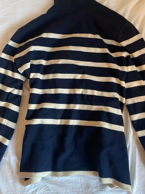 Marinblå randig polotröja från H&M - Snygg marinblå polotröja från H&M i storlek S med vita horisontella ränder. Tröjan har lång ärm och hög krage, perfekt för dig som gillar klassisk stil med en modern twist. Materialet känns mjukt och bekvämt mot huden.