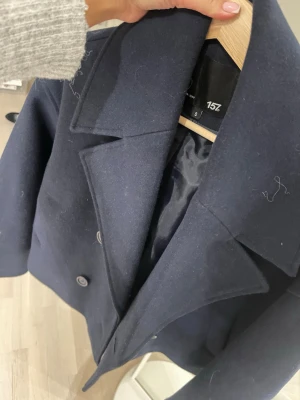 Mörkblå skepparkavaj från 157 - Säljer en stilren mörkblå skepparkavaj från 157 i storlek S. Jackan har breda slag, dubbelknäppning med fyra knappar och är tillverkad i ett tjockt ullmaterial. Perfekt för dig som gillar klassisk och snygg look med lite edge.