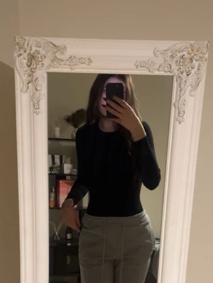 Svart långärmad bodysuit från Zara - Säljer en svart långärmad bodysuit från Zara med rund hals och tight passform. Toppen är enkel och stilren, perfekt att matcha med jeans eller kjol. Materialet är mjukt och stretchigt, vilket gör den bekväm att bära hela dagen.