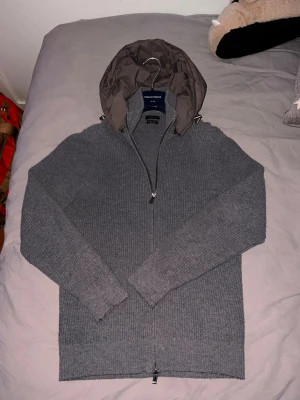Cardigan från Massimo Dutti - Säljer en grå stickad hoodie från Massimo Dutti med dragkedja och avtagbar huva . Cardiganen kostar 3500kr av ny men sälj inte längre och många vill ha den!   Pris kan diskuteras vid snabb affär