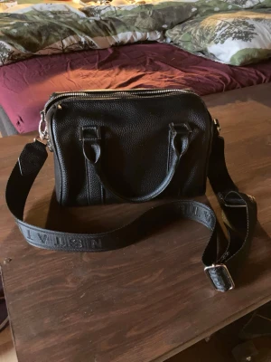 Svart axel/hand väska - Axelremmen har texten Urban Status broderat i svart, my let bra skick och endast använd några få gånger. Det går att ta bort det justerbara axelbandet och inuti väskan finns det p ena sidan en ficka med dragkedja och en till ficka på andra sidan utan dragkedja, fodret k väskan är också svart.