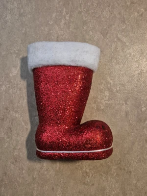 Julstövel - Säljer en röd glittrig julstövel med vit fluffig kant upptill. Stöveln har en rundad form och är dekorerad med glitter över hela ytan samt en vit linje vid sulan. Perfekt som dekoration till julen!
