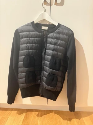 Moncler cardigan  - Svart Moncler cardigan med stickade cashmere ärmar och fyra framfickor i stickat material. Jackan har quiltad framsida, rund hals och dragkedja. Moncler-logga på vänster ärm. Nfc finns på loggan!        Pris kan diskuteras!