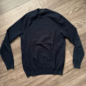 Mörkblå tröja från MNG MAN - Snygg mörkblå tröja från MNG MAN i klassisk modell med rund hals och långa ärmar. Tröjan är tillverkad i mjuk bomull och har ribbade muddar vid hals, ärmslut och nederkant. Perfekt för dig som gillar stilrena och enkla plagg. Den är lite urtvättad 