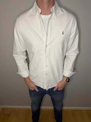 Vit slim fit skjorta från Ralph Lauren - Vit skjorta från Ralph Lauren i slim fit-modell, storlek L. Klassisk design med knappar framtill och broderad logga på bröstet. Tillverkad i mjuk bomull och har långärmade ärmar samt krage med knapp. Perfekt för dig som gillar stilrena och tidlösa plagg. Skick 9/10. Vi kan gå ner i pris vid snabb ovh smidig affär. /Studio II Resell 