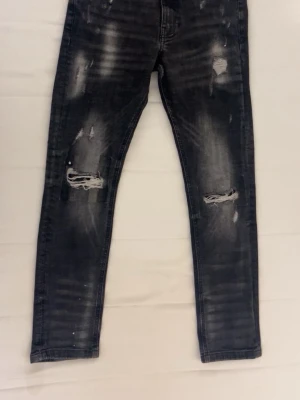 Supply & Demand svarta jeans M (barn size) - Svarta jeans från Supply & Demand med slitna detaljer och trasiga knän. Jeansen har en mörk tvätt med ljusare partier och ribbade effekter på baksidan av benen. Perfekt för dig som gillar en edgy streetstil.