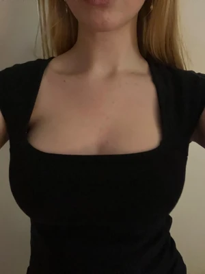 Svart ribbad topp med fyrkantig urringning - Säljer en svart ribbad topp med snygg fyrkantig urringning och korta ärmar. Modellen är croppad och sitter tight mot kroppen, perfekt att styla med jeans eller kjol. Materialet är mjukt och stretchigt, vilket gör den bekväm att bära hela dagen.