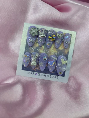 Hoshi (S);Medium Almond - Säljer ett set med lila lösnaglar i storlek S: 15 mm, 11,5 mm, 12 mm, 11 mm, 9 mm, dekorerade med silverdetaljer som rosetter, hjärtan, nalle, rosett, pärlor och holografiska stenar. Naglarna har en medium mandel form och är täckta med glitter och 3D-accessoarer för en extra glam look.