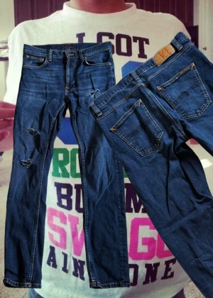 Mörkblå Nudie Jeans W29 L30 - Säljer ett par mörkblå jeans från Nudie Jeans i storlek W29 L30. Klassisk femficksmodell med orangea sömmar och slitna detaljer på benen. Jeansen har rak passform och är tillverkade i robust denim med snygg tvätt.