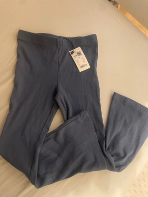 Blå ribbade byxor från 157 - Snygga blå ribbade byxor från 157 i mjukt och stretchigt material. Modellen har en rak passform med utsvängda längst nere, elastisk midja och diskret ribbad struktur som ger en cool vibe. Perfekta att matcha med en oversized hoodie eller t-shirt. Barn till tjejer, storlek 120 
