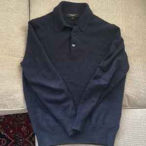 Mörkblå kashmir pikétröja Lawrence Grey - Exklusiv mörkblå pikétröja från Lawrence Grey i 100% kashmir. Tröjan har klassisk krage, knäppning med två knappar och långa ärmar. Perfekt för dig som vill ha en stilren och lyxig look med mjuk känsla.