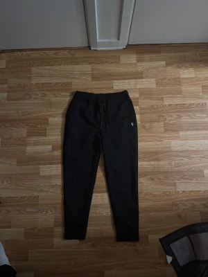 Svarta mjukisbyxor Polo Ralph Lauren - Svarta mjukisbyxor från Polo Ralph Lauren med klassisk logga broderad på benet. Byxorna har snörning i midjan, ribbade muddar vid benslut och är gjorda i mjukt bomullsmaterial. Perfekta för chill eller träning.