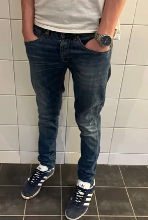 Dondup George blå jeans slim fit - Snygga Dondup George jeans i klassisk blå tvätt med slim fit passform. Modellen har fem fickor, låg midja och raka ben med lätt tapered siluett. Jeansen är tillverkade i slitstarkt bomullsmaterial. Perfekta för en chill och stilren look.