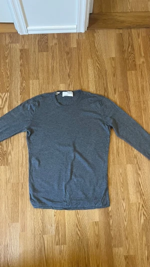 Grå långärmad tröja från Selected Homme - Snygg grå långärmad tröja från Selected Homme i storlek L. Tröjan har en enkel och stilren design med rund hals och är tillverkad i mjuk bomull. Perfekt för dig som gillar en clean look och vill ha något bekvämt att slänga på sig.