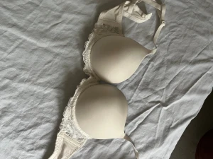 Vit spetskantad bh  - Säljer en vit bh med spetsdetaljer längs sidorna. Axelbanden är justerbara och bh:n har klassisk hakknäppning bak. Storlek 70A. Push up
