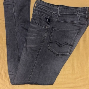 Replay Anbass slim fit jeans grå - Snygga Replay Anbass slim fit jeans i mörkgrå tvätt med klassiska fem fickor och svarta sömmar på bakfickorna. Jeansen har normal midja och smal passform, tillverkade i mjukt jeanstyg för en bekväm känsla. Perfekt för dig som gillar stilrena och moderna jeans.