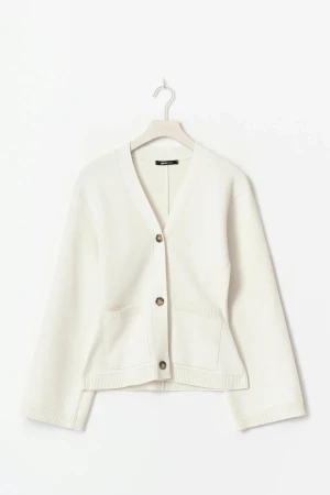 Vit stickad kofta  - Säljer en fräsch vit stickad kofta från Gina Tricot i bomull. Koftan har v-ringning, tre snygga knappar framtill och två praktiska fickor. Modellen är normal i passningen och har långa ärmar med ribbade muddar. Perfekt för lager-på-lager under vår och höst. Se Defekt på sista bilden. 