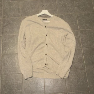 Beige kofta från LMTD med knappar - Snygg beige kofta från LMTD i storlek S, passar dig som gillar enkel och clean stil. Koftan har långa ärmar, v-ringning och knappar framtill. Materialet känns mjukt och är perfekt för lager-på-lager under hösten och vintern. 13-14 men skulle säga att den passar större