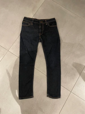 Nudie jeans mörkblå - Tja säljer nu ett par feta raw denim/mörkblå jeans från Nudie  med slim passform och klassisk femficksdesign. Jeansen har orange guldiga sömmar, knapp och dragkedja framtill  Perfekt för dig som gillar en clean och stilren look. Skicket är helt perfekt som nytt ungefär och storleken är w29 l30 passar dig som är runt 167-175 lång skulle jag tro!! Har du några övriga frågor är de bara att höra av sig🙌🏼mvh em_resell🤩