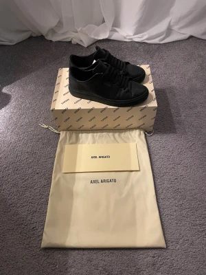 Svarta sneakers Axel Arigato  ”croco” - Säljer ett par svarta sneakers från Axel Arigato med croco-präglat skinn och snygga svarta snören. Klassisk låg modell med rund tå och platt sula. Kommer med originalkartong och dustbag. Perfekt för dig som gillar stilrena och exklusiva detaljer.
