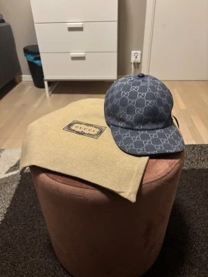 Blå Gucci keps med GG-mönster. PÅSE INGÅR - Säljer en snygg blå keps från Gucci med klassiskt GG-mönster i ljusgrått. Bästa kvalité, helt ny och påse ingår. Kepsen har böjd skärm, justerbar rem bak i skinn och är tillverkad i bomullscanvas. Perfekt för dig som vill ha en lyxig och trendig accessoar med tydlig designerstil. 