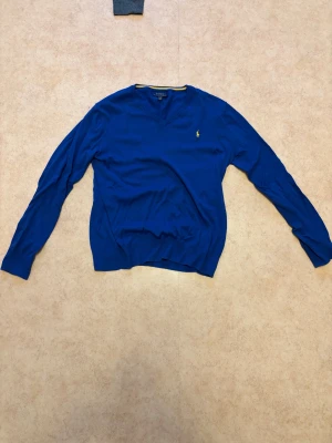 Blå v-ringad tröja från Polo Ralph Lauren - Snygg blå v-ringad tröja från Polo Ralph Lauren med det klassiska broderade logot på bröstet. Storlek 170 men passar perfekt om du har storlek S