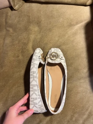 Michael Kors ballerinaskor med logga - Snygga ballerinaskor från Michael Kors i ljusbeige /vita med MK-mönster och guldfärgad logodetalj framtill. Helt nya och äkta!!!🙌🏼