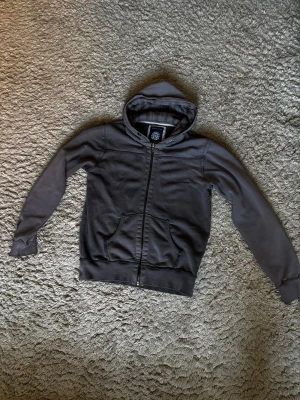 Grå hoodiejacka från Batistini - Grå hoodiejacka från Batistini i bomullsmix med hel dragkedja, kängurufickor och fodrad huva med rutigt mönster på insidan. Perfekt för chill dagar och enkel att matcha med jeans eller joggers‼️🔥buda gärna!