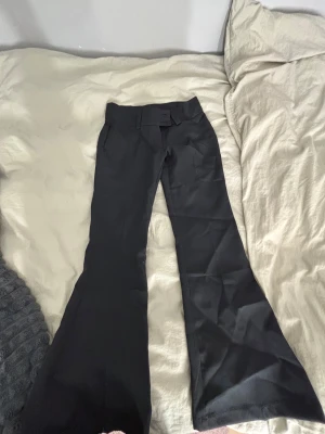 Svarta bootcut-byxor från RYVLS - Snygga svarta bootcut-byxor från RYVLS i storlek 152. Byxorna har breda benslut, klassisk midja och bälteshällor. Materialet är slätt och känns bekvämt mot huden. Perfekt för dig som gillar en stilren och trendig look.