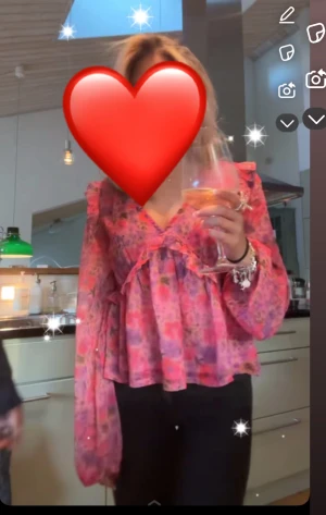 Blommig rosa blus med volang - Säljer en blommig blus i rosa och lila toner med v-ringning och volangdetaljer framtill. Blusen har långa, lätt puffade ärmar med resår vid handlederna och är tillverkad i ett tunt, transparent material som ger en luftig känsla. Perfekt för dig som gillar färg och romantiska detaljer.