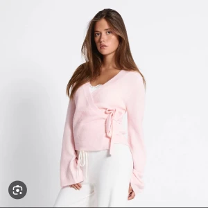 Ljusrosa omlottkofta Willow lager 157 - Supersöt rosa  omlottkofta från lager 157 med knyt i sidan och v-ringad hals. Koftan är stickad och har långa ärmar med lite lösare passform. Perfekt att slänga på sig över ett linne för en chill och trendig look.