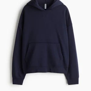 Mörkblå hoodie - Säljer en stilren oversized mörkblå hoodie med klassisk huva och stor magficka. Tröjan har en loose passform och är tillverkad i mjuk bomull. Storlek M. Helt ny i förpackning säljs pga glömt returnera beställning i tid