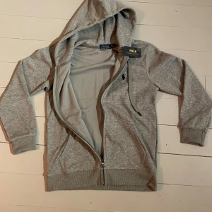 Polo Ralph lauren zipup hoddie  - Snygg grå hoodie från Polo Ralph Lauren med dragkedja och huva. Aldrig andvänd bara testat på en gång så är i väldigt bra skick (liten i passformen). Kan sänka pris 