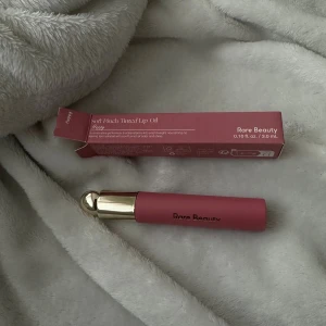 Rare Beauty Soft Pinch Tinted Lip Oil - Säljer en Soft Pinch Tinted Lip Oil från Rare Beauty i färgen Happy. Tuben är matt rosa med guldfärgat lock och rymmer 3 ml. Oljan ger en mjuk rosa ton och glans till läpparna med en lätt och återfuktande formula.
