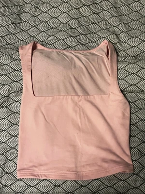 Ljusrosa ärmlös linnetopp - Säljer en ljusrosa linnetopp med fyrkantig urringning och ärmlös design. Toppen har en clean och enkel look, perfekt att styla med jeans eller kjol. Materialet känns mjukt och stretchigt mot huden. Passformen är normal och toppen är croppad i modellen.