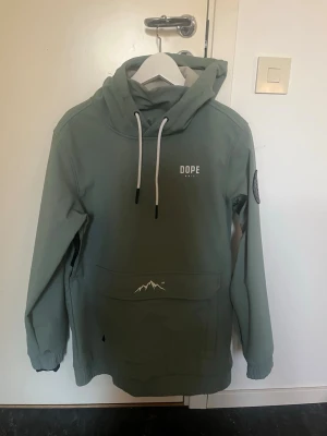 Turkos skidjack från Dope - Snygg grön turkos skidjacka från Dope med huva och vita snören. Jackan har en stor magficka med bergsdetalj. Jag säljer min snygga dope jacka då den inte kommer till andvänding. Jag har inte andvänt den någon gång bara provat den så den är som ny och den är i storlek S😊