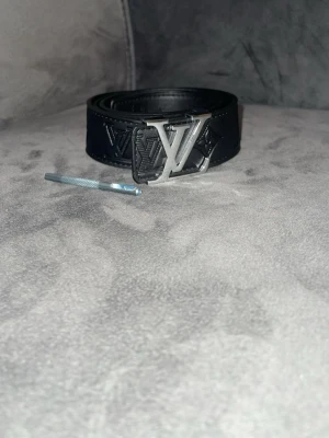 Svart bälte med silver logo - Fin bälte med inga skador storlek 110 cm .