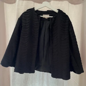 Svart strukturerad kappa från H&M - INTRESSEKOLL!! Säljer en svart kappa från H&M i storlek 38. Jackan har ett unikt strukturerat tyg med vågiga detaljer och är helfodrad. Den har en rak och lite lös passform, perfekt för dig som vill ha något stilrent men ändå speciellt.💗