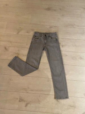 Grå jeans från Kappahl, storlek 152 - Snygga grå jeans från Kappahl i rak modell med klassiska fem fickor och knappstängning. Jeansen är tillverkade i mjukt bomullsmaterial och har en neutral grå färg som passar till det mesta. Perfekt för dig som gillar enkel och stilren look.Grå jeans Denim Byxor Slim fit Rak modell Normal midja Stretch Bekväma Mjuk denim Vardagliga Trendiga Mode Stilrena Klassiska Vintage Retro Begagnade Bra skick Som nya Hållbara Kvalitet Premium Design Unika Sällsynta Garderobsrensning Fynd Rea Erbjudande Herr 