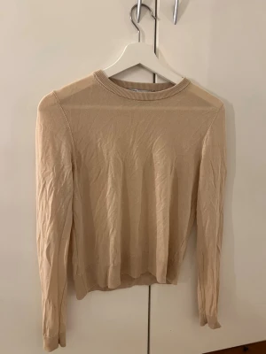 Beige långärmad tröja från Zara - Säljer en stilren beige långärmad tröja från Zara. Tröjan har rund hals med ribbad kant och är tillverkad i mjuk bomull. Passformen är normal och den är perfekt för lager-på-lager under hösten och våren. Enkel design utan mönster eller extra detaljer.