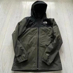 Svart och olivgrön vindjacka North Face - Säljer en stilren vindjacka från The North Face i svart och olivgrönt. Perfekt för blåsiga dagar och outdoor-aktiviteter. Bara att höra av sig vid intresse 