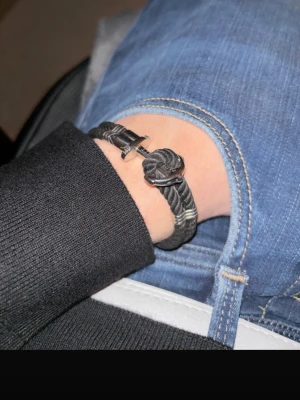 Svart armband från Paul Hewitt - Snyggt svart armband med grov tvinnad design och ett metallfärgat ankare som lås. Armbandet har silverfärgade detaljer och passar perfekt för dig som gillar marina accessoarer. Materialet är troligtvis syntet med metallspänne.