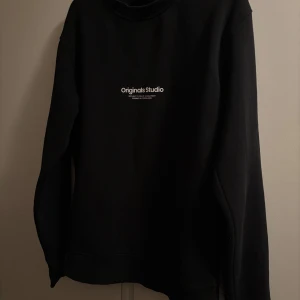 Svart sweatshirt från Jack & Jones XS - Svart sweatshirt från Jack & Jones Originals Studio i storlek XS. Tröjan har ett stilrent tryck på bröstet och är tillverkad i mjuk bomull med långärmad passform. Perfekt för dig som gillar enkel och clean streetstyle.