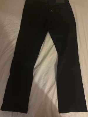Svarta Levis jeans 514 - Säljer ett par svarta Levis jeans med klassisk rak-passform. Jeansen har fem fickor och en diskret Levis-logga på bakfickan. Materialet är slitstarkt jeans och färgen är helsvart, vilket gör dem enkla att matcha med olika stilar.