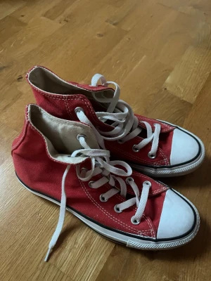 Röda Converse (höga) - Säljer ett par klassiska röda höga Converse med vit tå och vita snören. Skorna har en rund tå och platt sula. Perfekt för dig som gillar ikoniska sneakers med cool retrostil.