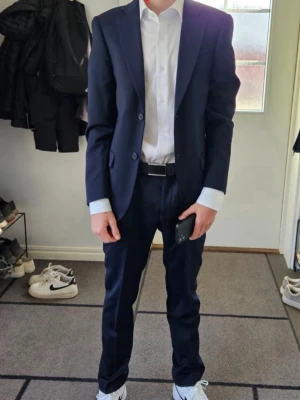 Mörkblå kostym Dressmann slim fit - Säljer en stilren mörkblå kostym från Dressmann med slim fit passform. Kavajen har klassisk design med två knappar och matchande kostymbyxor. Ingår även en vit extra slim fit skjorta i bomullsstretch. Perfekt för dig som vill ha en snygg och modern look. Använd max 5 ggr. Hela köpt för ca. 2700