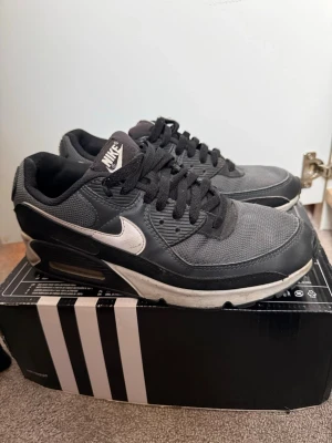 Nike Air Max svart/vit sneakers 42 - Svarta Nike Air Max sneakers med vit swoosh och detaljer. Skorna har snörning, platt sula och rund tå. Ovandelen är i syntet och mesh för bra ventilation. Klassisk Air Max-dämpning i sulan för extra komfort. Perfekt för dig som gillar streetwear och sportig stil.