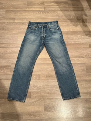 Blå jeans från Weekday - Säljer ett par klassiska blå jeans från Weekday med rak passform och fem fickor. Jeansen har en normal midja och är tillverkade i slitstarkt bomullsmaterial. Perfekt för dig som gillar en enkel och tidlös stil.